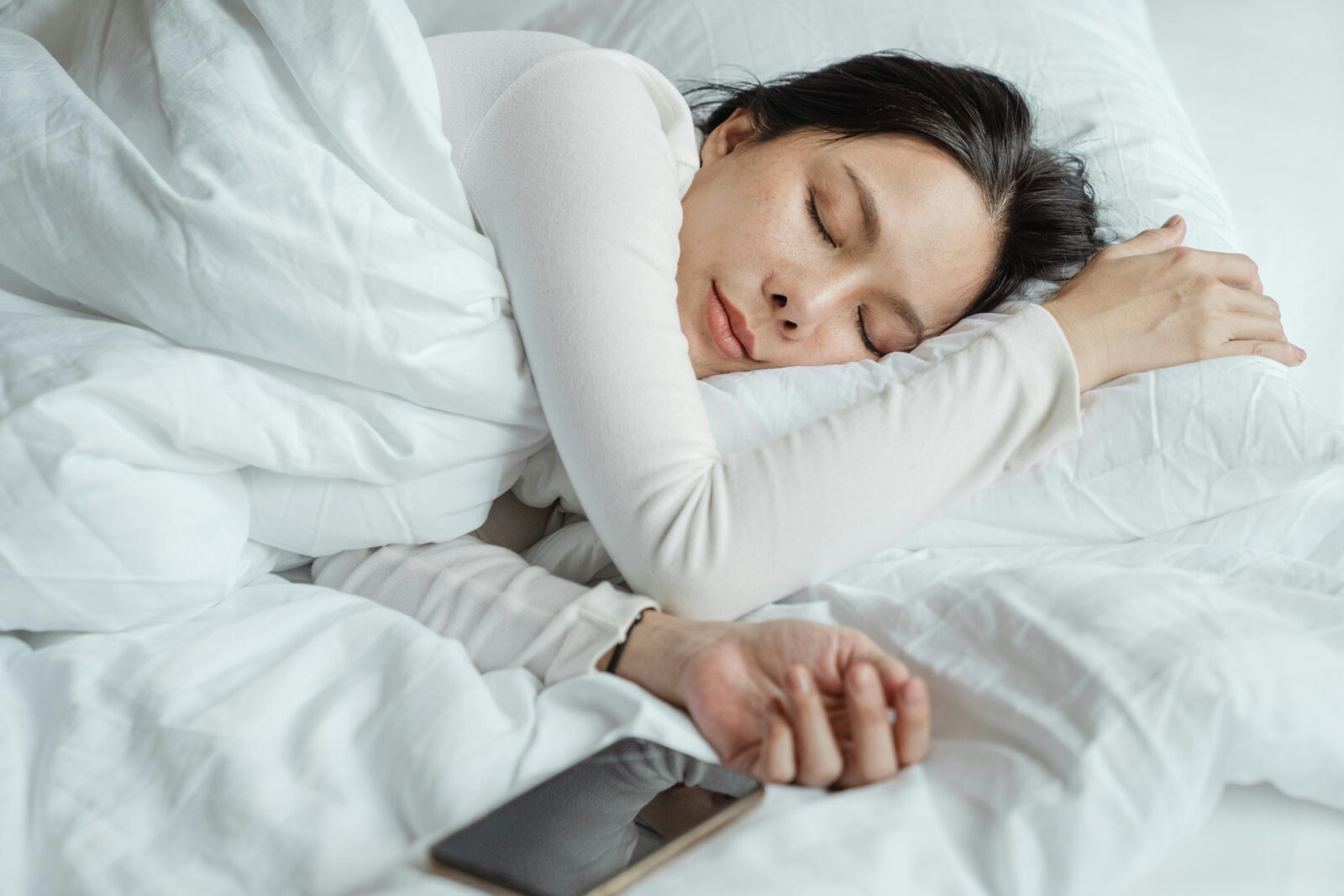 Woman asleep in bed with a smartphone beside her.