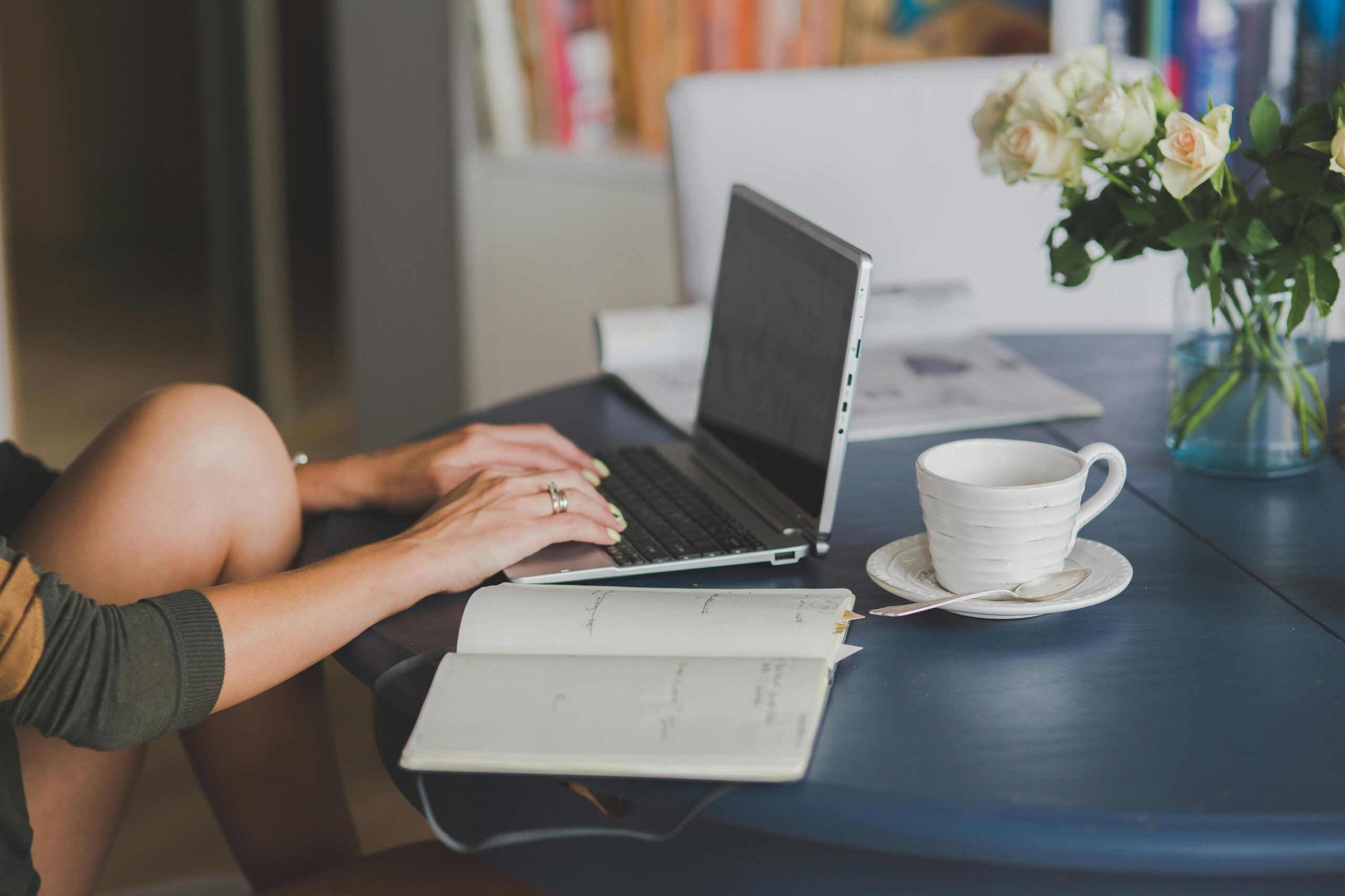 Person working on a laptop with a notepad, coffee cup, and flowers on the table. Breaking down to tasks for managing adhd