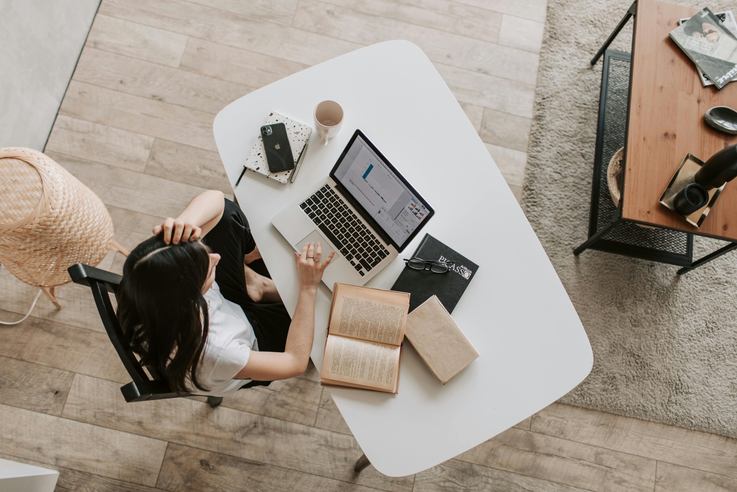 Top-down view of a person working at a laptop at a minimalist desk with an open book and notebook nearby.