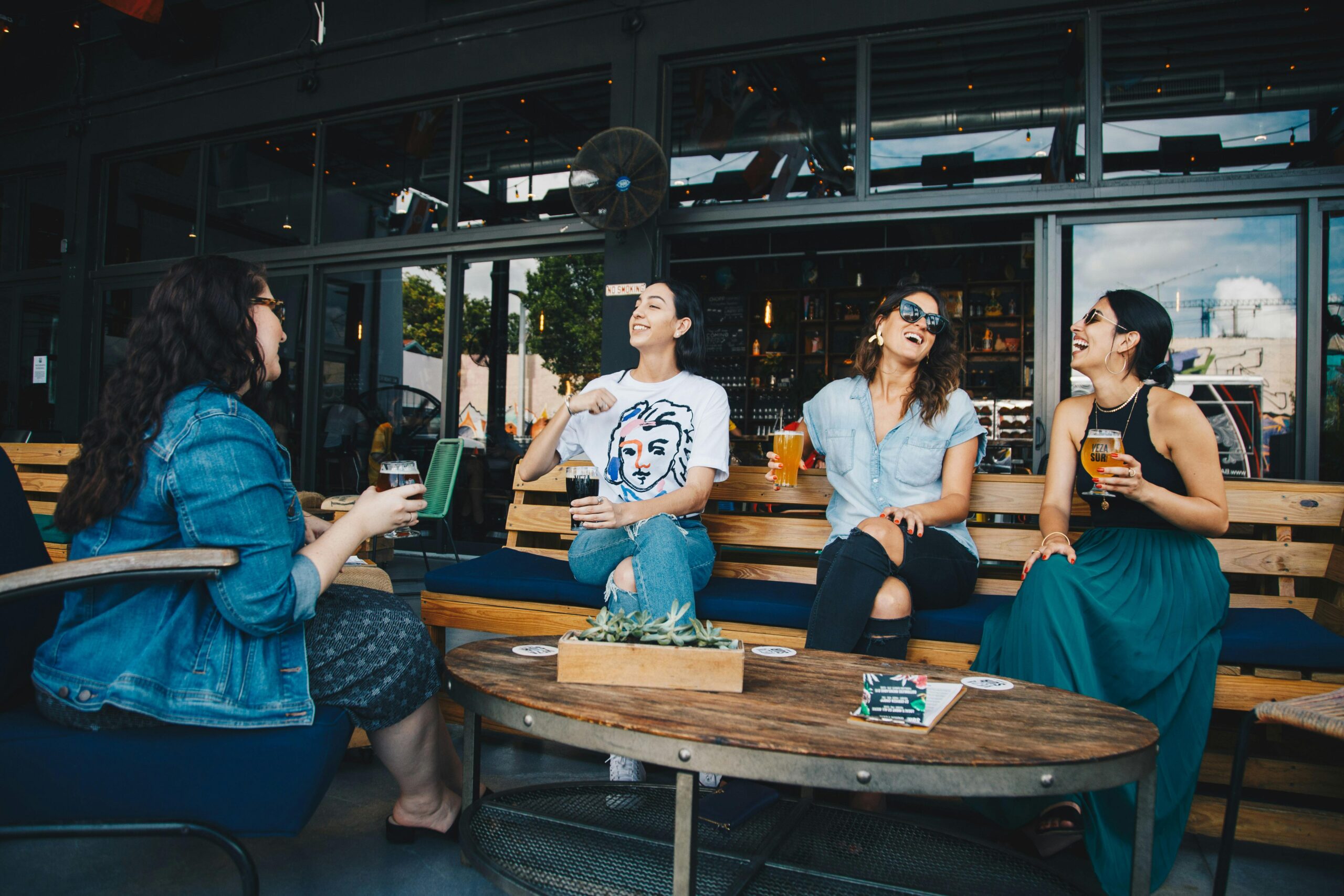 Four friends laugh and enjoy drinks at an outdoor bar with a modern aesthetic.