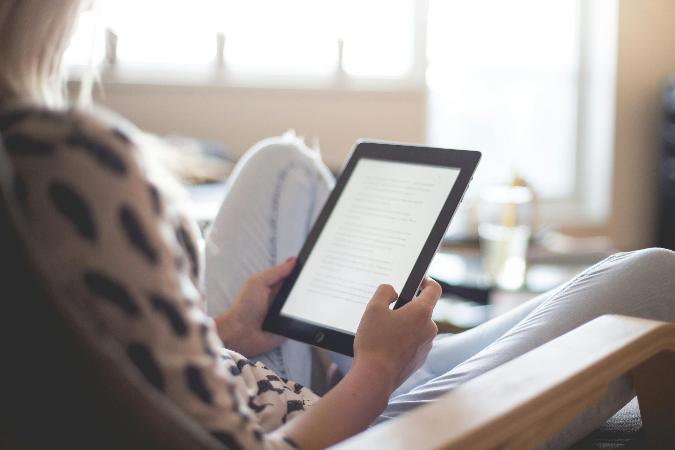 A person lounging on a chair, reading an e-book on a tablet, in a bright, softly lit room to avoid creative burnout